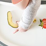 baby hand reaching for a slice of avocado on a tray.