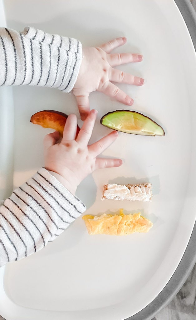 baby hands on a tray with pieces of food cut into pieces for baby led weaning.