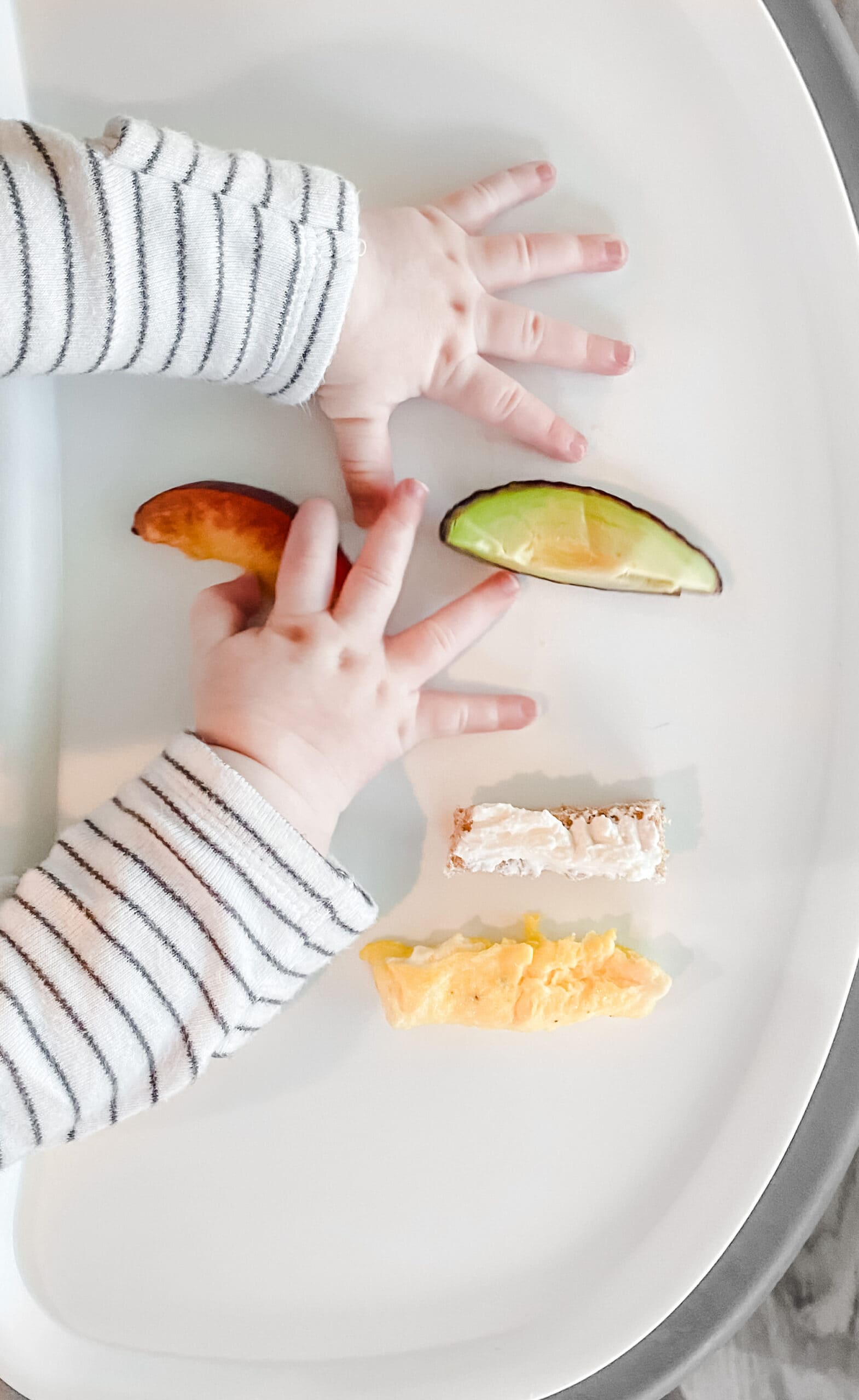 baby hands on a tray with pieces of food cut into pieces for baby led weaning.