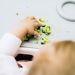 baby hand grabbing pieces of broccoli on a tray.