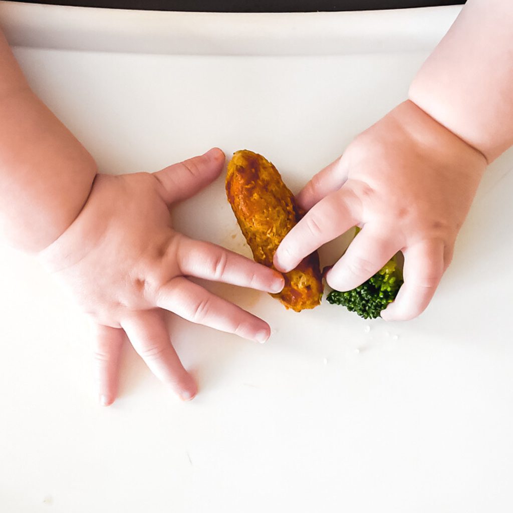 baby hands grabbing a meatball and broccoli on a high chair tray