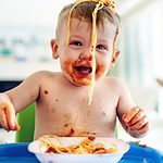 baby with spaghetti on his head smiling in a high chair.