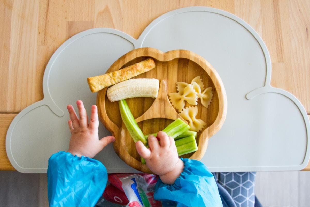 baby hands getting food off of a bamboo plate on a cloud shaped mat.