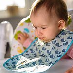 baby in a whale bib spitting out food.
