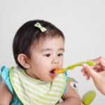 baby leaning toward a spoonful of food.