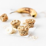 baby banana baked oatmeal muffins with banana slices next to them on top of parchment paper with a banana in the background.