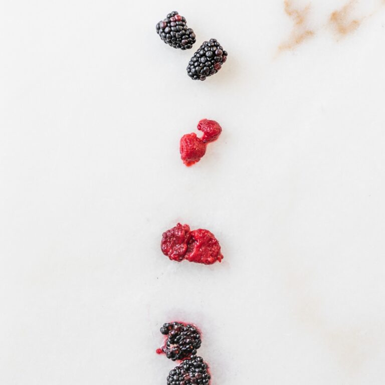 various forms of blackberries and raspberries lined up on a white marble background