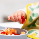baby hand picking up a piece of strawberry with a pincer grasp.