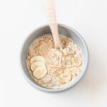 baby bowl of peanut butter banana overnight oats topped with peanut butter and banana slices with a pink baby spoon in it.