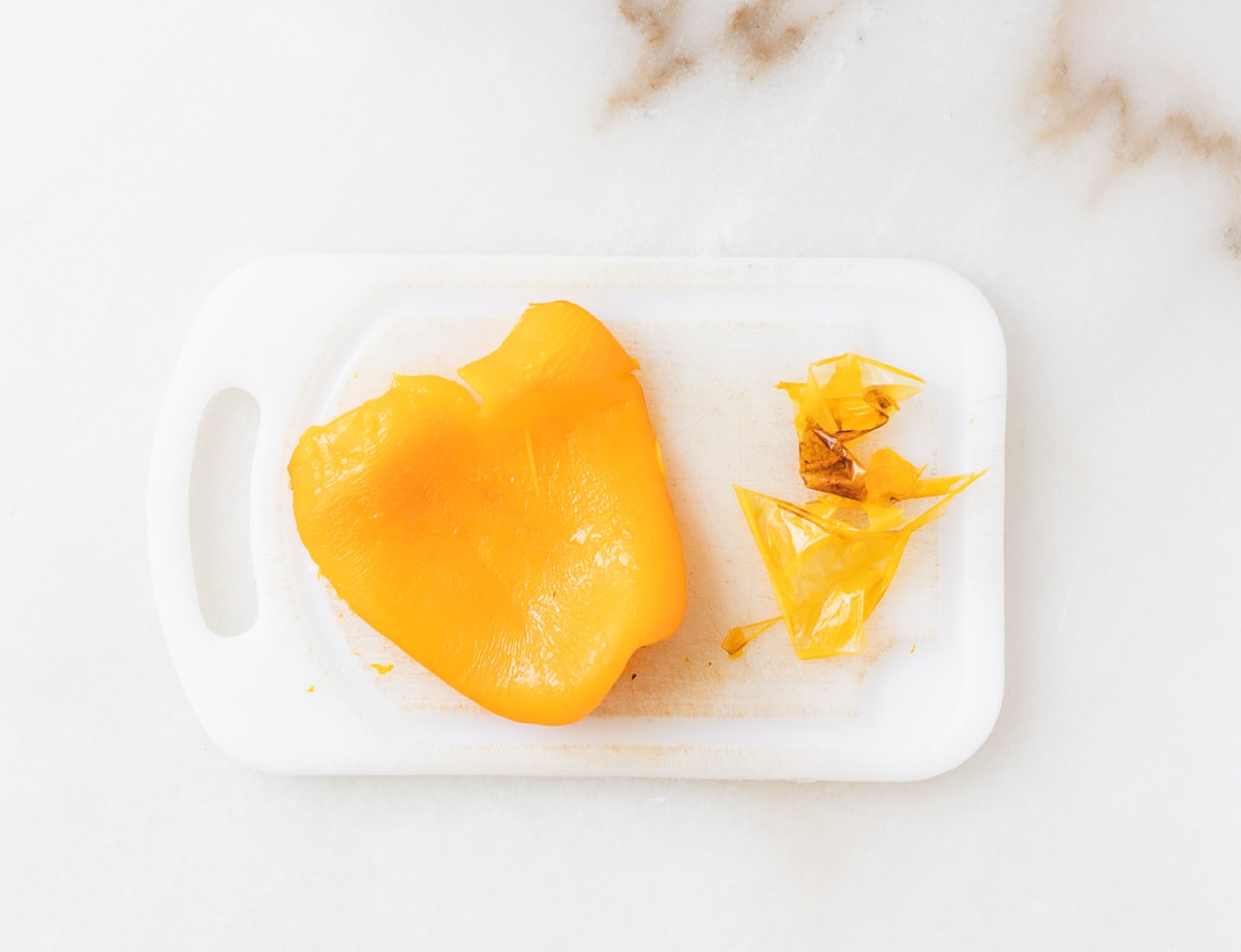 cooked bell pepper half with skin peeled off on a white cutting board.