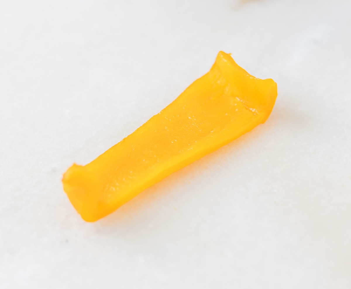 cooked orange bell pepper strip on a white background.