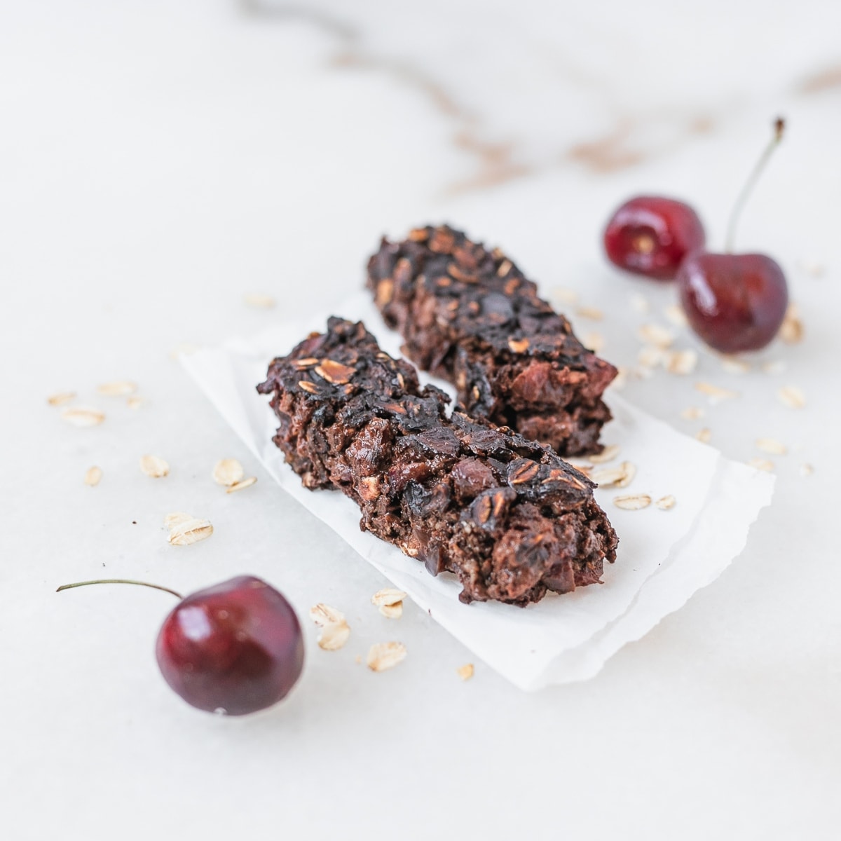 cherry chocolate baked oatmeal fingers for baby led weaning on a piece of parchment with cherries around them.