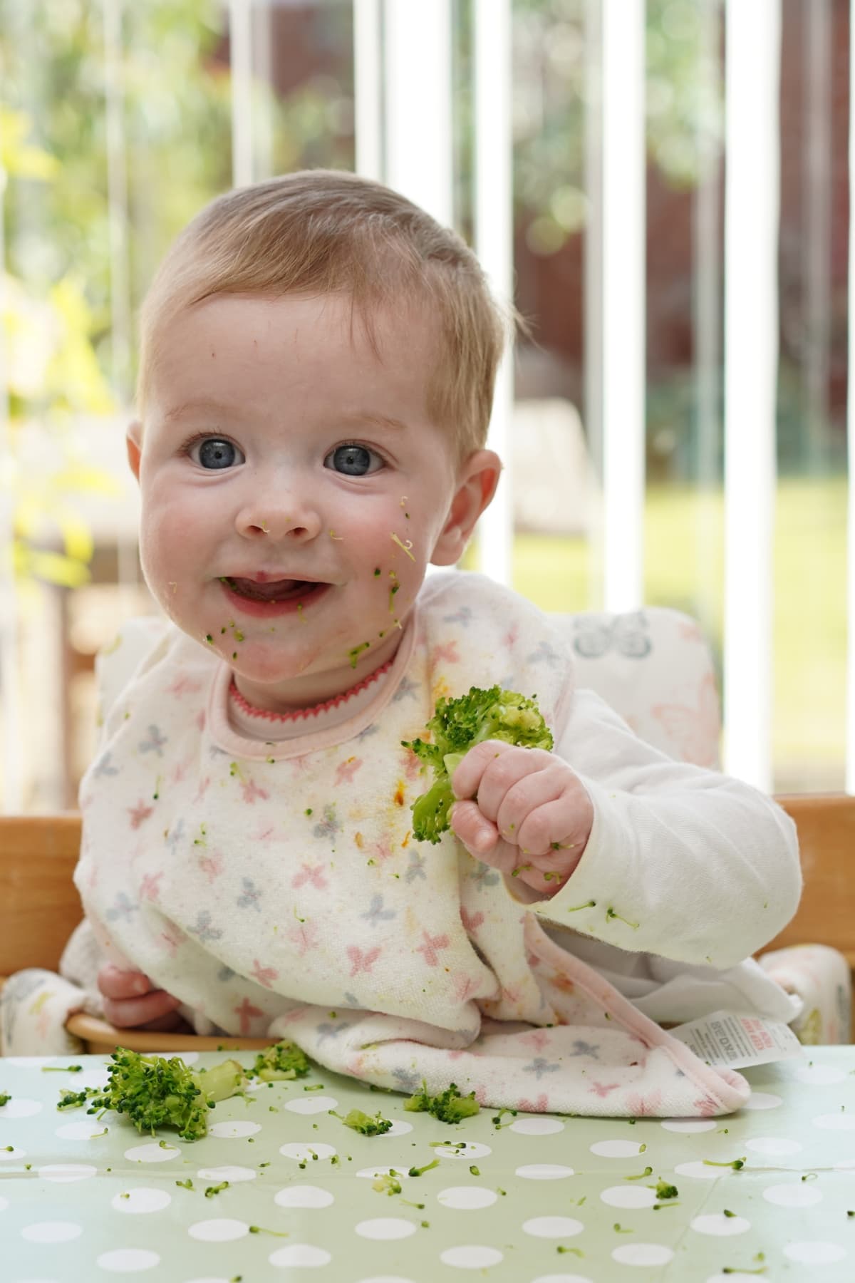 baby girl in bib holding broccoli with palmar grasp.