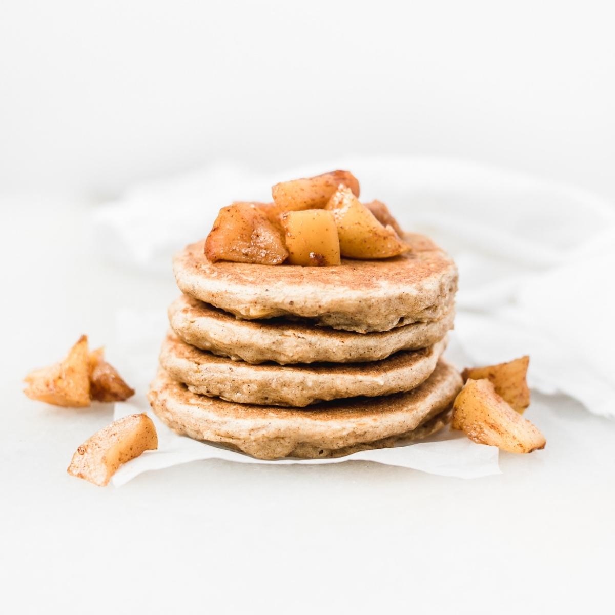4 baby apple pancakes stacked on a piece of parchment with cooked cinnamon apple pieces on top.