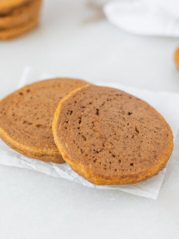 two baby sweet potato pancakes on a piece of parchment paper.