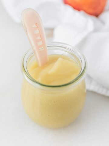 glass jar of applesauce with a pink baby spoon in it.