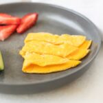 omelet cut into strips for baby on a grey plate with strawberries.