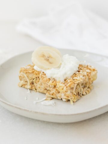 square of tropical baked oatmeal topped with yogurt and banana slices.