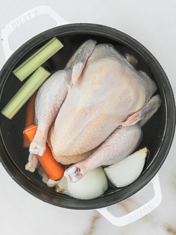 whole chicken with celery, carrots and quartered onion covered in water in a dutch oven.