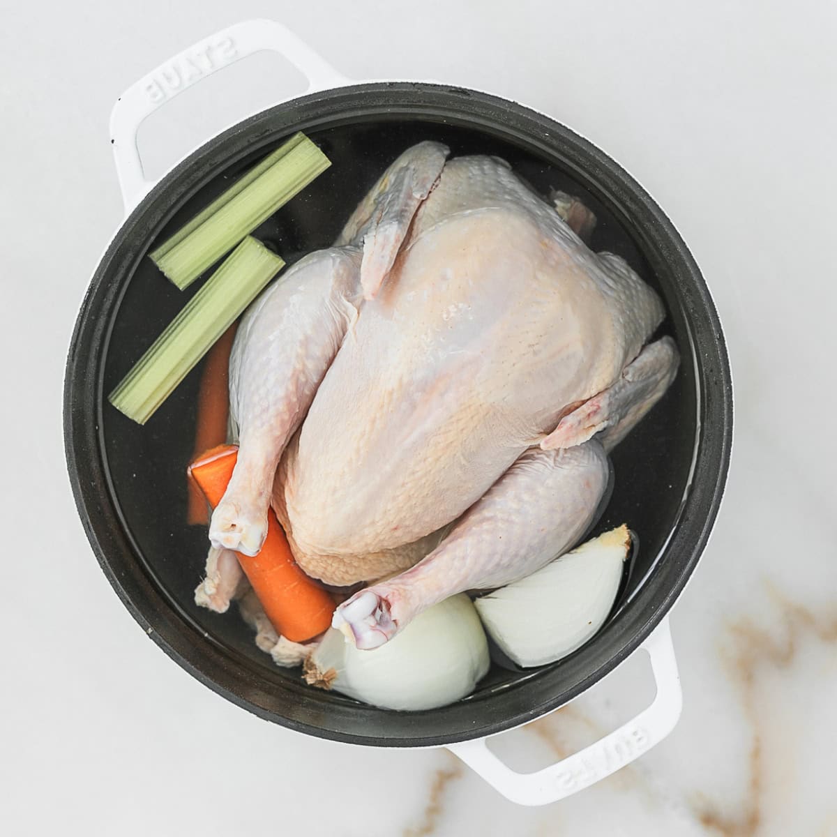 whole chicken with celery, carrots and quartered onion covered in water in a dutch oven.