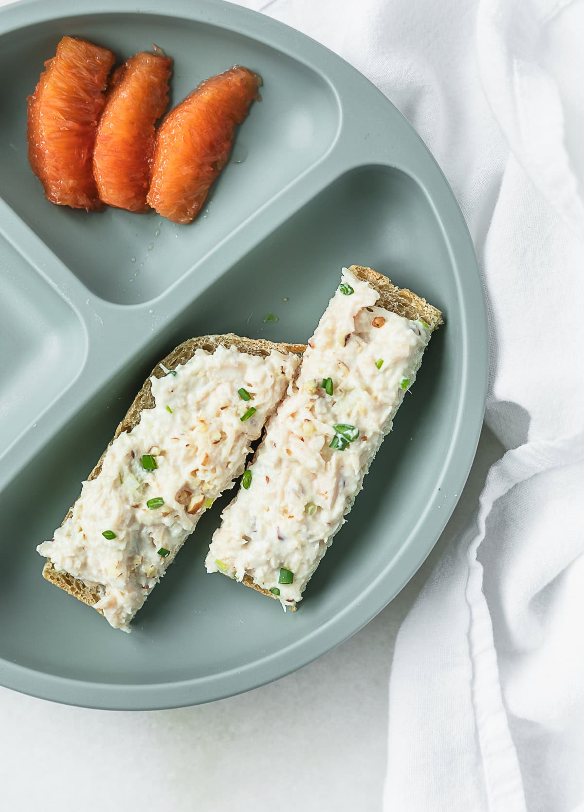 two baby bread fingers spread with baby chicken salad on a baby plate with orange segments.