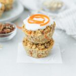 two carrot cake baked oatmeal muffins stacked with yogurt and a carrot swirl on top of one.