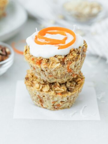 two carrot cake baked oatmeal muffins stacked with yogurt and a carrot swirl on top of one.