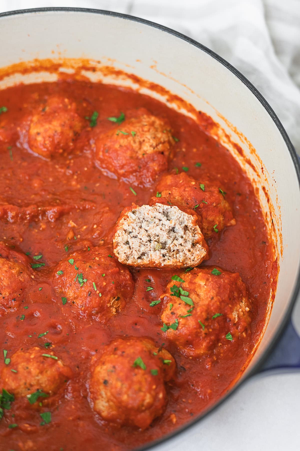 chicken ricotta meatballs in tomato sauce in a dutch oven with a half meatball on top to show inside.