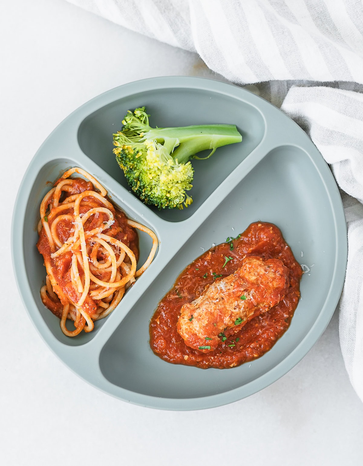 green baby plate with chicken ricotta meatball in a  finger shape for baby led weaning, broccoli, and spaghetti.
