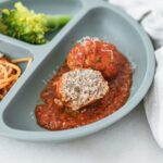 baby chicken meatball and halved meatball in tomato sauce on a baby plate.