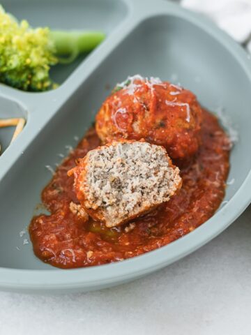 baby chicken meatball and halved meatball in tomato sauce on a baby plate.