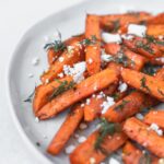 closeup of roasted carrots with dill and feta on a plate.