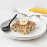 square of banana quinoa breakfast bake topped with banana on a small plate with a black spoon.