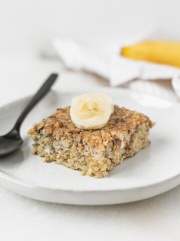square of banana quinoa breakfast bake topped with banana on a small plate with a black spoon.