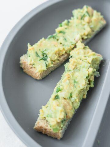 mashed chickpea avocado salad on two toast fingers on a baby plate.