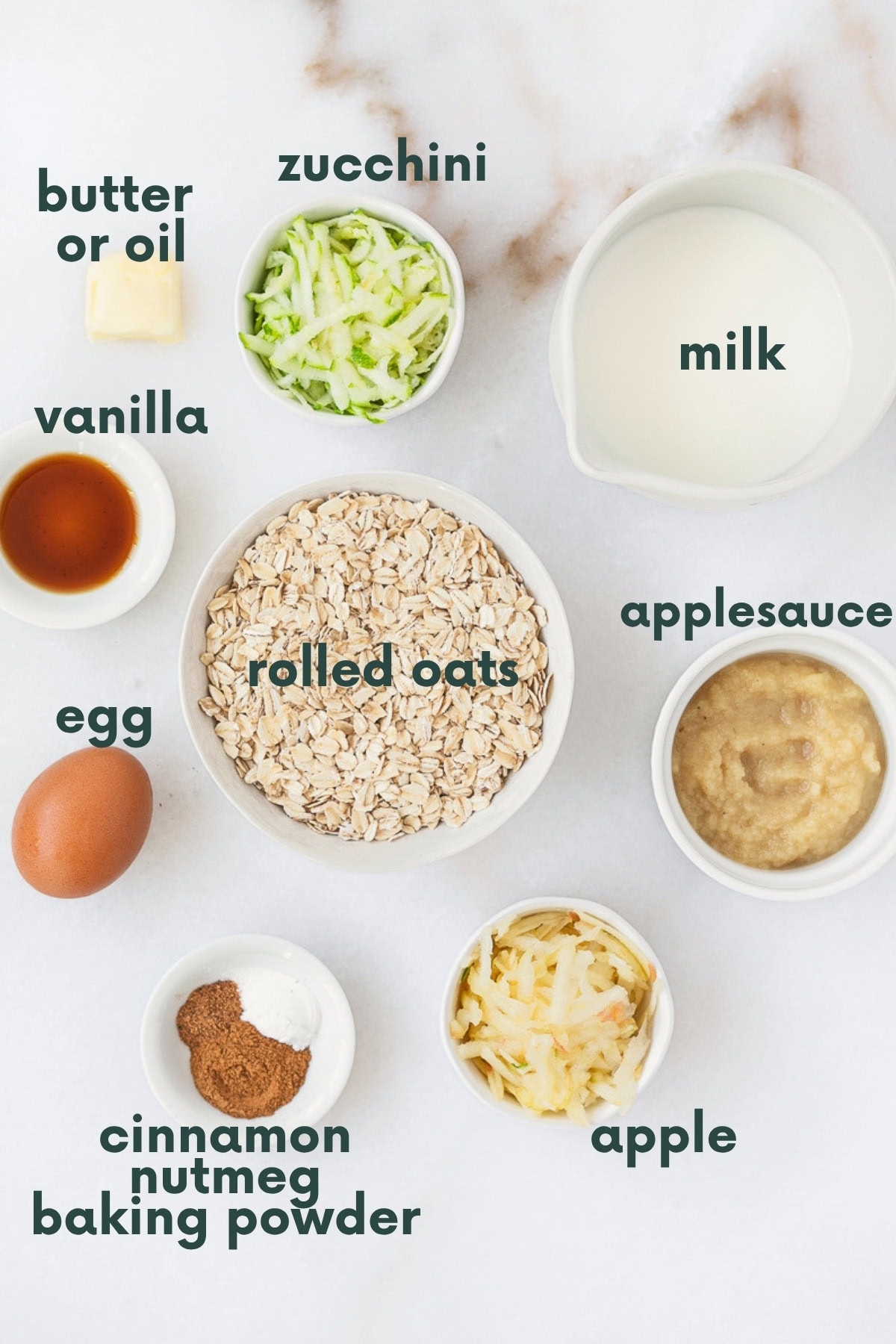 ingredients for zucchini apple baked oatmeal cups in bowls on a white marble background with text overlay. 