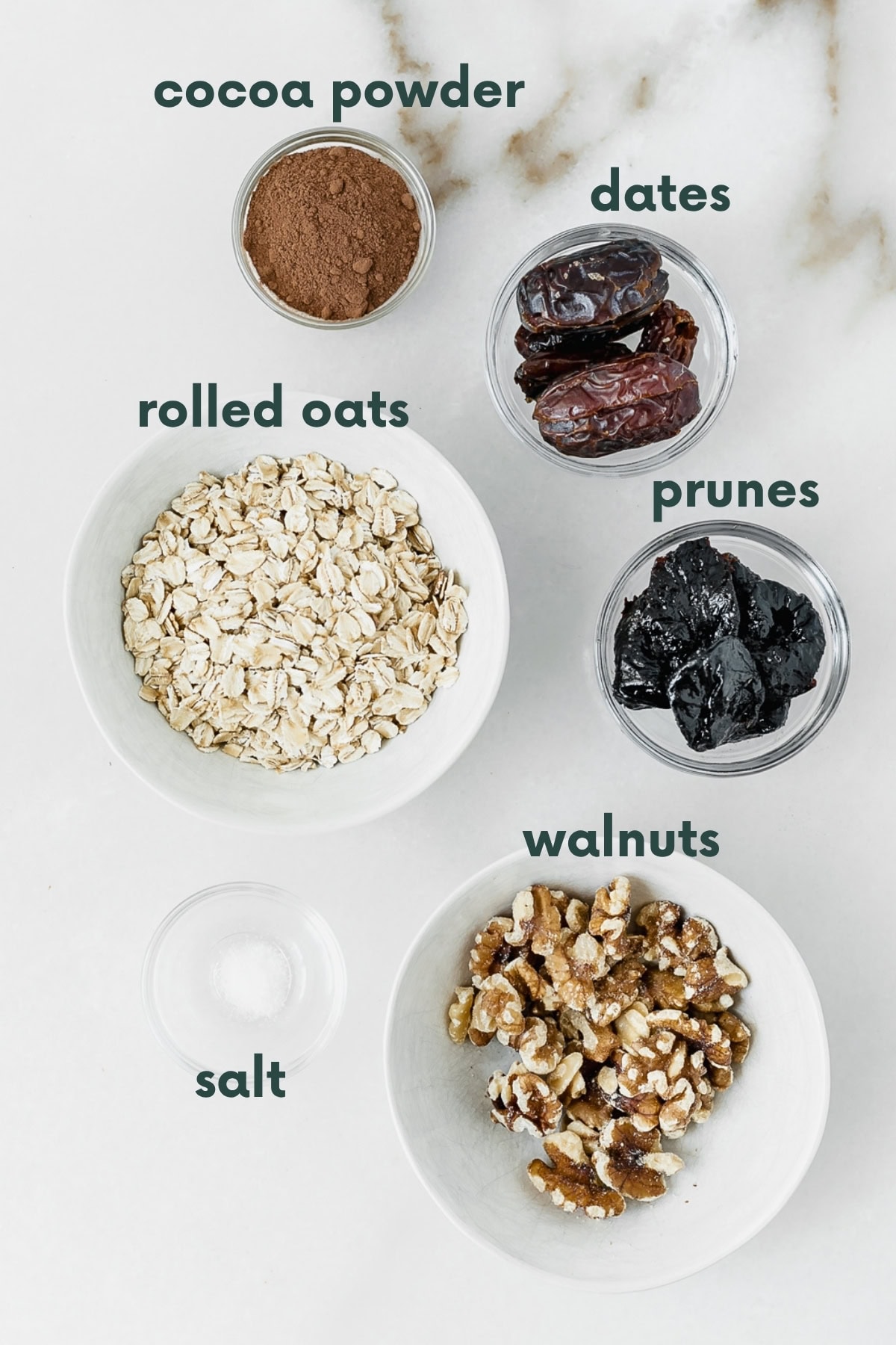 ingredients needed for prune brownie balls in bowls on a white marble backdrop with text overlay.