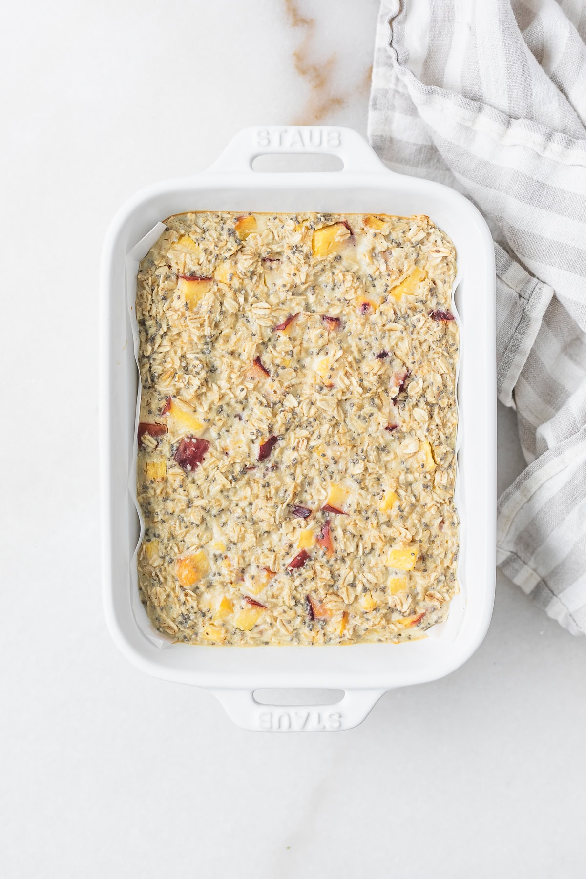 peaches and cream baked oatmeal in a baking dish with a striped towel next to it.