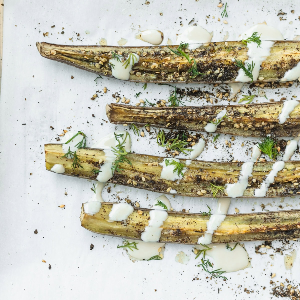 wedges of zaatar roasted eggplant drizzled with tahini sauce and topped with fresh herbs on parchment.