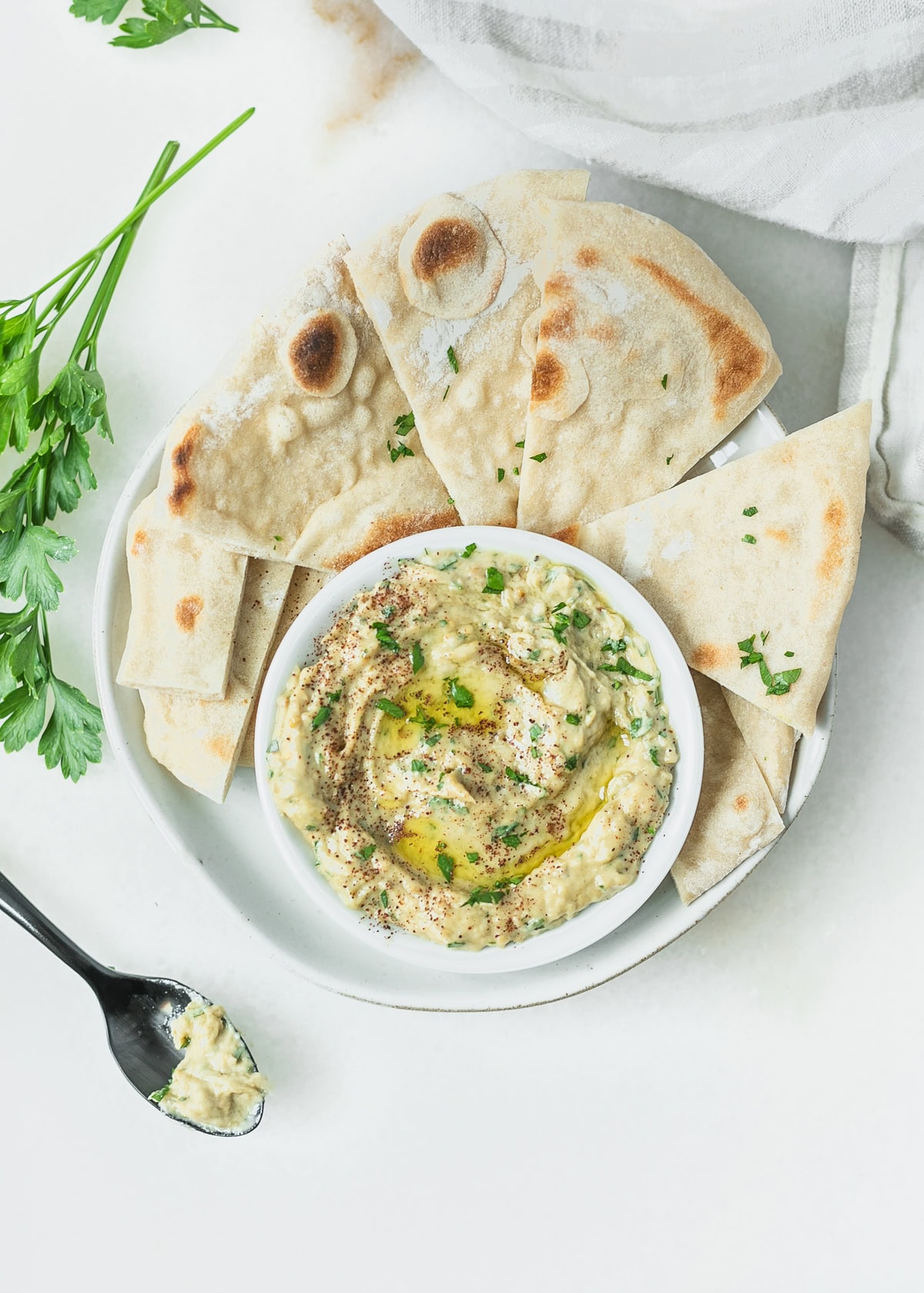 roasted eggplant dip on a small dish surrounded by pita wedges on a plate.