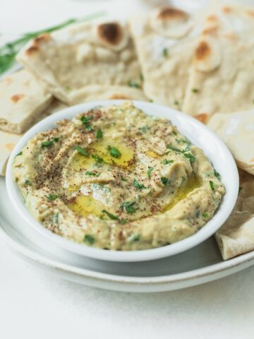 small bowl of babaganoush surrounded by pita wedges on a plate.