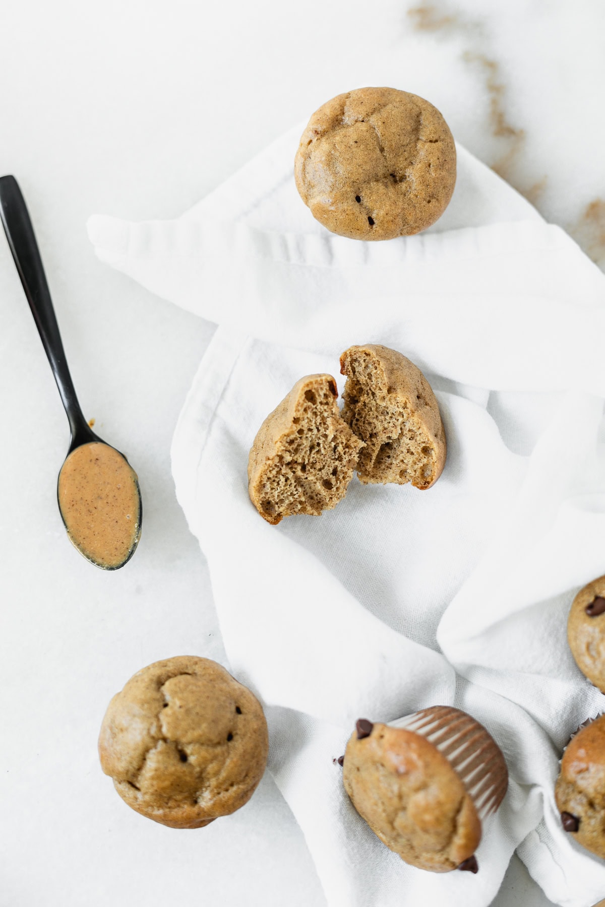 mini peanut butter banana protein muffin cut in half surrounded by more muffins and a spoon of peanut butter.