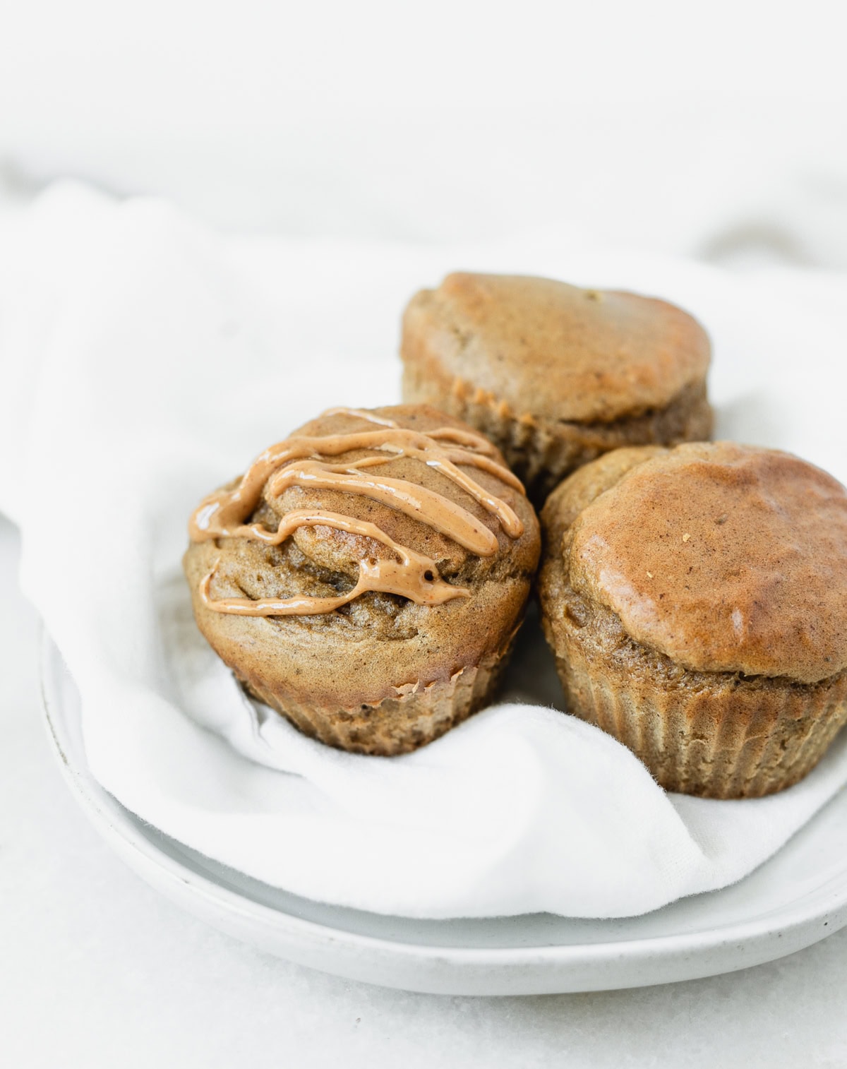 three banana peanut butter cottage cheese muffins on a small plate with peanut butter drizzled on one.