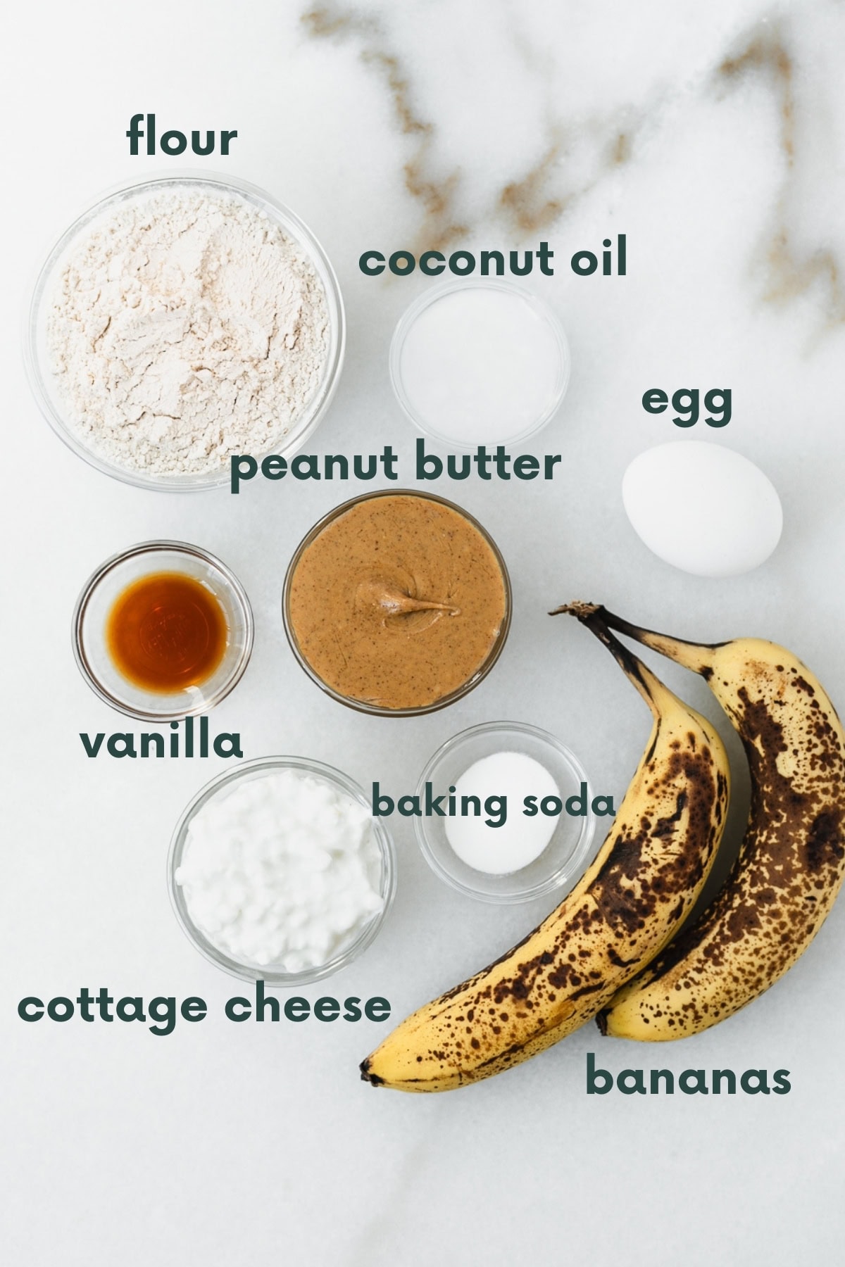 ingredients needed to make peanut butter banana protein muffins on a white marble background with text overlay.