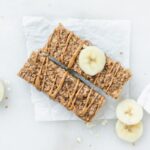 two soft baked oatmeal bars drizzled with almond butter and toped with a banana slice.