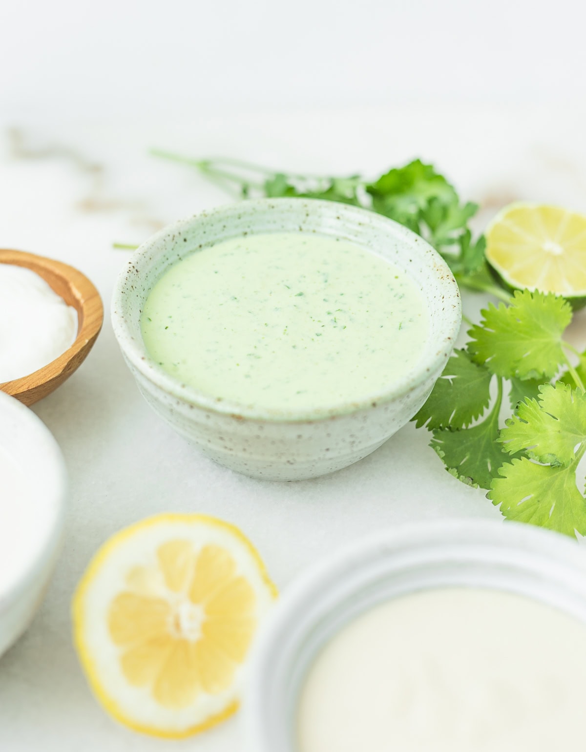 herby green tahini sauce in a stoneware bowl with herbs and lime behind it.