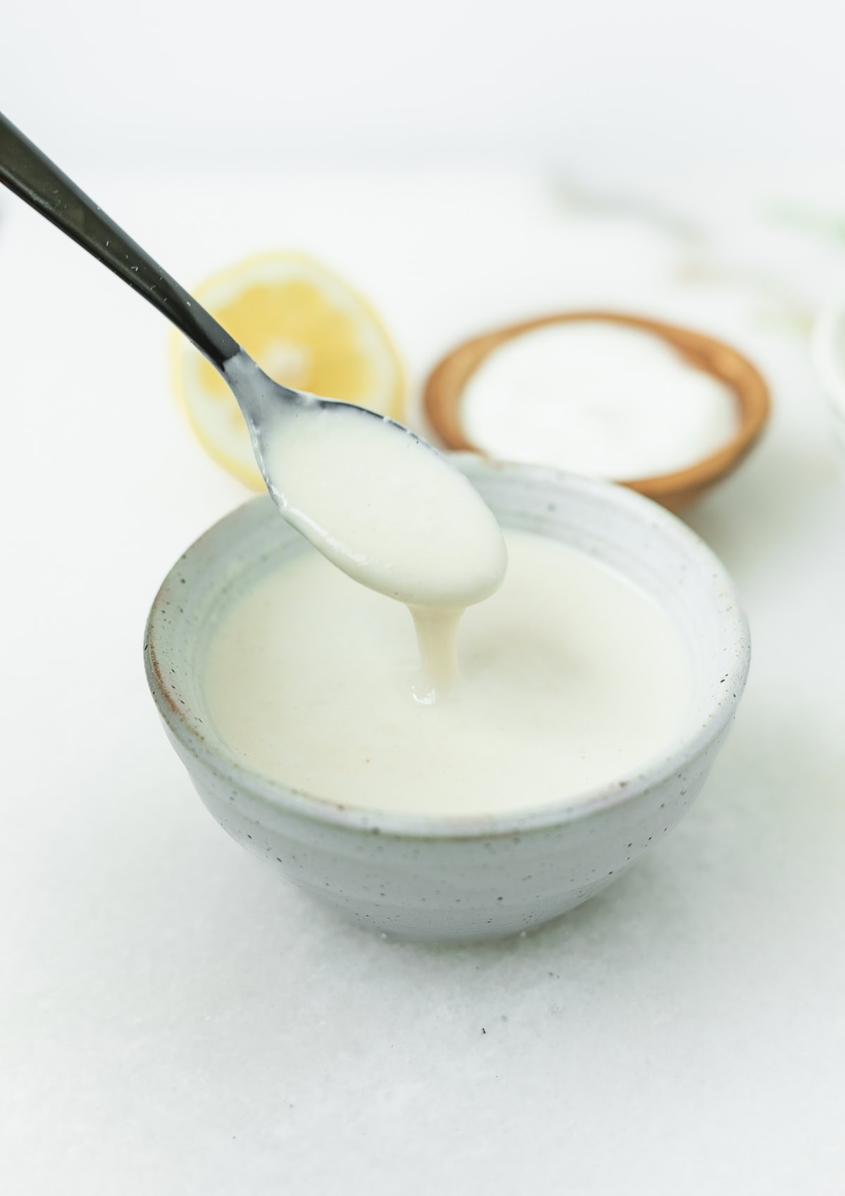 spoon lifting yogurt tahini sauce from a small stoneware bowl.