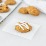 baby pumpkin chickpea cookie with yogurt drizzle on a square of parchment with more cookies in the background.
