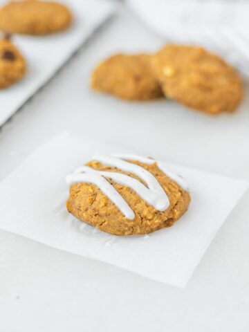 baby pumpkin chickpea cookie with yogurt drizzle on a square of parchment with more cookies in the background.