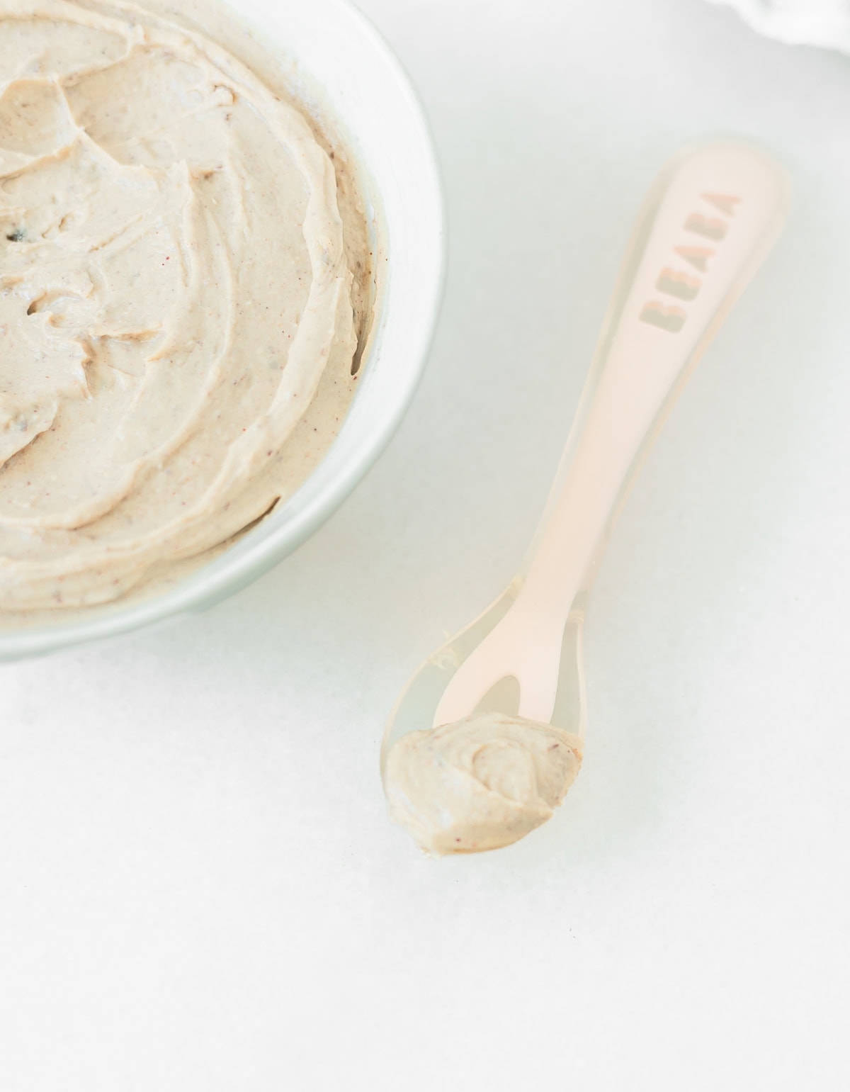pink baby spoon with peanut butter cottage cheese in it next to a bowl of peanut butter cottage cheese.